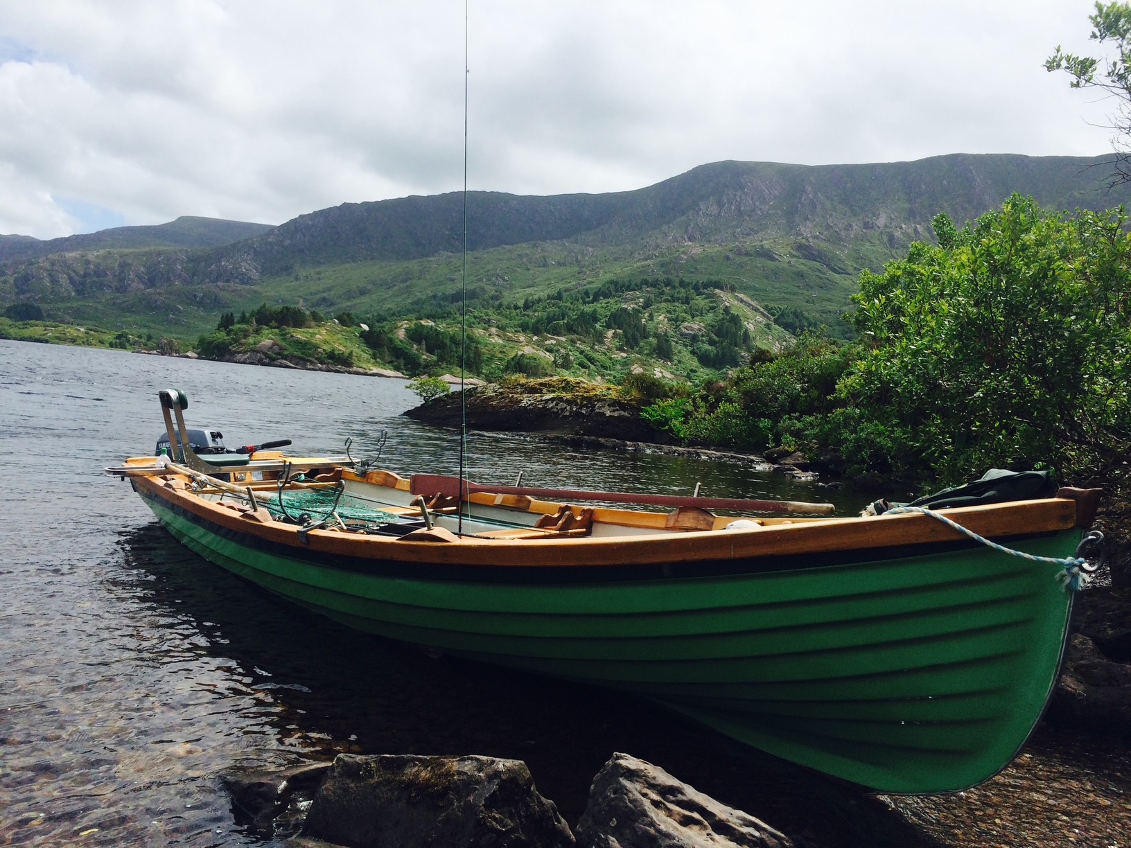 A scenic view of a calm Irish lough surrounded by green hills, with a small boat pulled up on the shore